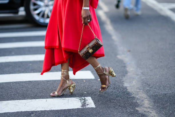 Guest wears gold large earrings, a red polar oversized puffy sleeves / belted coat, a red matching polar asymmetric midi skirt, a gold large ring, a...