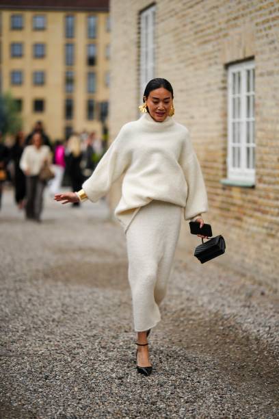 Guest wears gold large earrings, a white latte wool turtleneck pullover, a white latte wool long skirt, a black shiny leather handbag, black shiny...