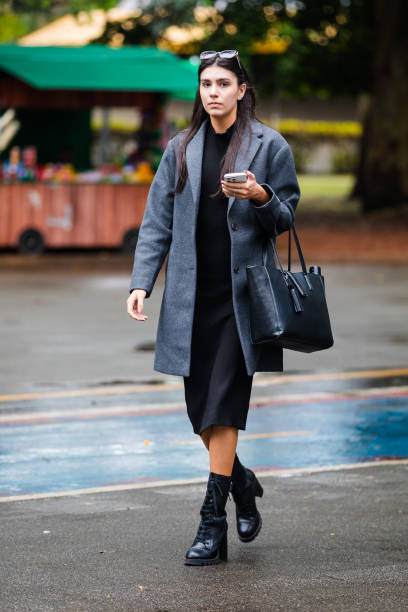 Guest wears gray overcoat, black dress, black high-heeled boots, black leather tote bag, sunglasses at Sao Paulo Fashion Week 2024 N58 - Street Style...