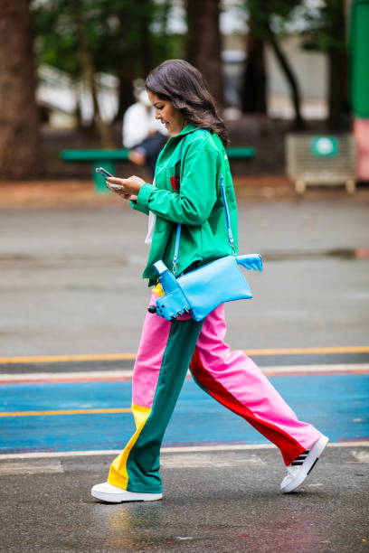 Guest wears green jacket, multicolor pants , white sneakers, blue dog-shaped bag at Sao Paulo Fashion Week 2024 N58 - Street Style at Parque...