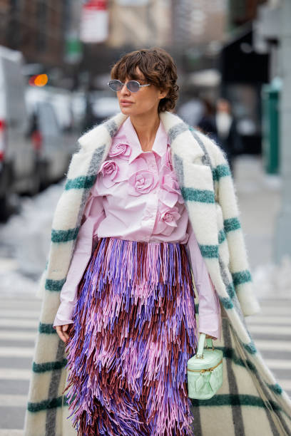 Guest wears green white checkered coat, pink blouse with appliquéd flowers, fringed pink purple skirt outside Michael Kors during New York Fashion...