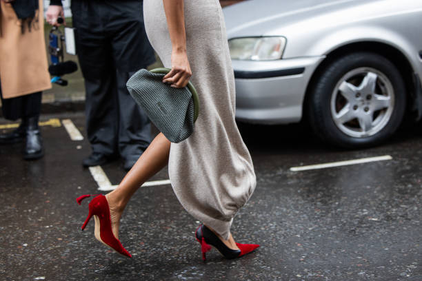 Guest wears grey green blue clutch, red heels, grey dress outside JW Anderson during London Fashion Week February 2024 on February 18, 2024 in...