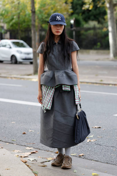 Guest wears grey peplum top with matching long skirt, blue New Era hat, blue bag, brown decorated sneaker, outside Rokh, during Womenswear...