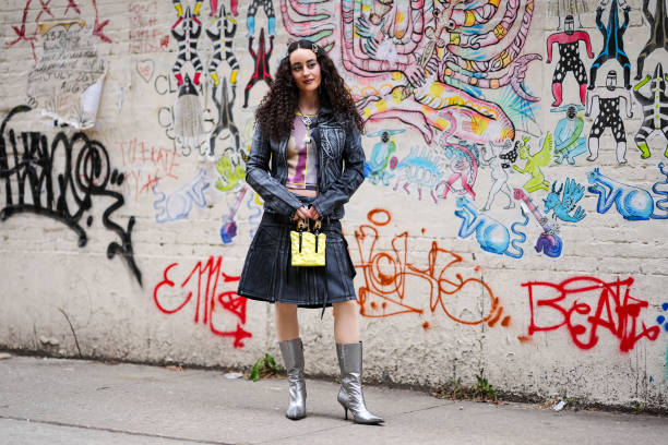 Guest wears hair pins with pearl details, a silver necklace, a grey and purple crop top with prints and yellow striped details / tie and dye, a black...