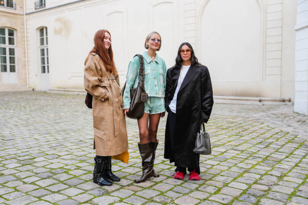 Guest wears light brown belted trench coat, shiny black belted laced boots leather shoes. Violet Grace Atkinson wears light blue sunglasses, silver...