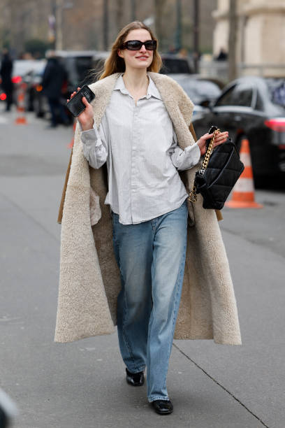 Guest wears light grey striped shirt, brown suede coat with fur inside, light wash jeans, black Chanel bag, outside Chanel, during the Womenswear...
