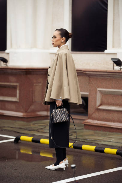 Guest wears long black skirt, beige trench coat, white shoes and Dior bag during the 10th season of the Visa Fashion Week Almaty on October 16, 2024...