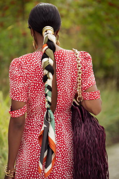 Guest wears long red dress with polkadots, burgundy bag with tassels, golden earrings and braid braided with scarf outside the Marimekko show during...