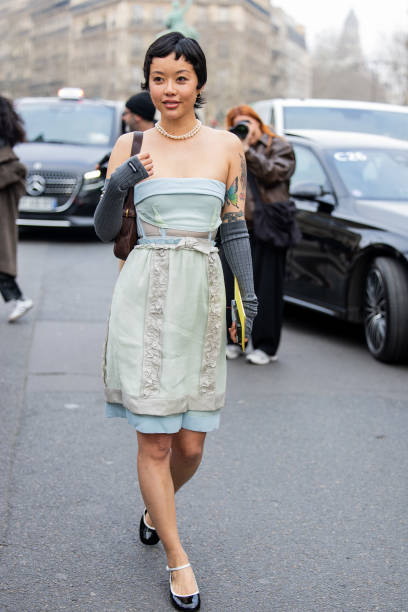 Guest wears mint green off shoulder top, skirt, grey gauntlets, brown bag outside Miu Miu during the Womenswear Fall/Winter 2025/2026 as part of...