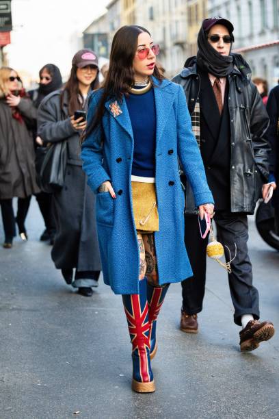 Guest wears orange sunglasses, a yellow teddy mini skirt, a blue sweater, a gold necklace, silver necklaces, a light blue teddy coat, an english flag...