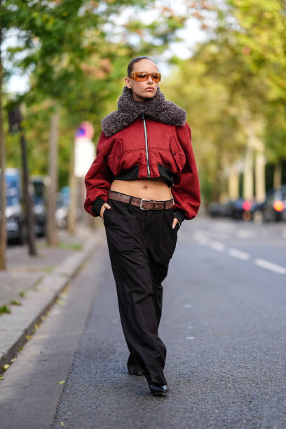 Guest wears orange sunglasses, dark red bomber jacket with dark brown fluffy collar, shiny dark brown leather belt, black loose pants, outside...