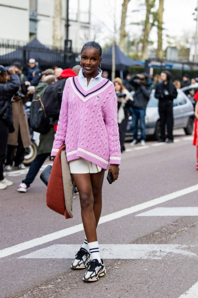 Guest wears pink v neck knit, pleated mini skirt, white button shirt, white socks, sneakers outside Lacoste during the Womenswear Fall/Winter...