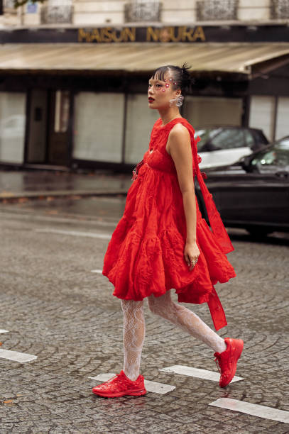 Guest wears red asymmetric dress, white laced tights and red sneakers outside The Cecilie Bahnsen show during Womenswear Spring/Summer 2025 as part...