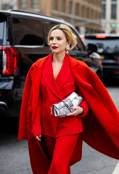 Guest wears red blazer, coat, silver bag, pants outside Michael Kors during New York Fashion Week on February 11, 2025 in New York City.