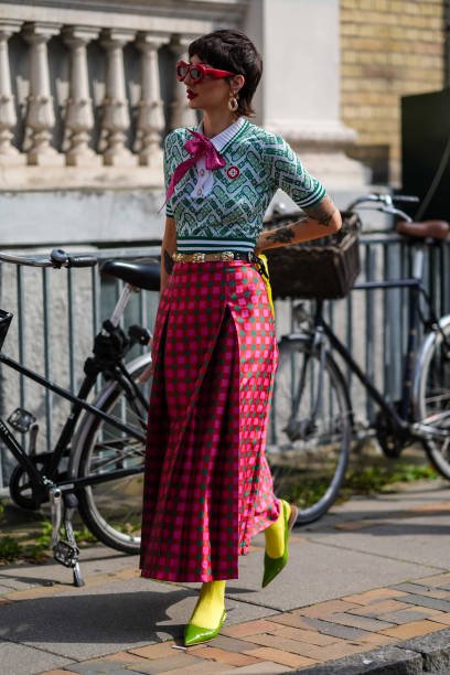 Guest wears red sunglasses, gold earrings, light green dark green pattern short sleeve shirt with hot pink bow, gold belt, dark pink hot pink green...