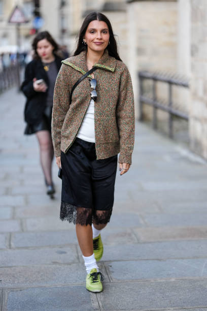 Guest wears silver earrings, dark brown pattern oversized unzipped cardigan jacket, white top, black sunglasses in top, shiny black crossbody leather...