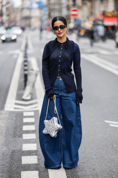 Guest wears star shaped Chanel bag, wide leg dark blue denim jeans, button up knit outside Akris during the Womenswear Fall/Winter 2024/2025 as part...