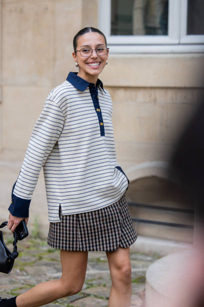 Guest wears striped polo shirt with long sleeves, skirt, bag, glasses outside Ganni during the Womenswear Fall/Winter 2025/2026 as part of Paris...