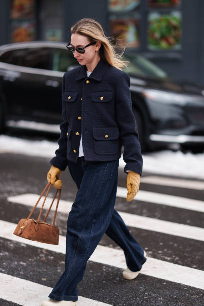 Guest wears sunglasses, a blue military jacket with golden buttons, blue flared denim pants / jeans , orange gloves, a brown bag, outside Ulla...