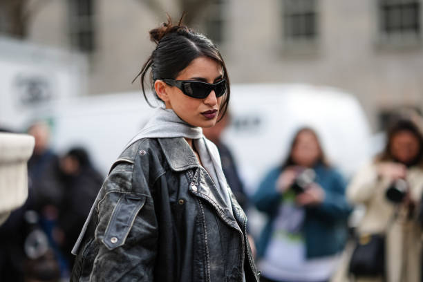 Guest wears sunglasses, a gray scarf, a black oversized biker leather jacket , a black t-shirt , black underwear on top of black tights, outside...