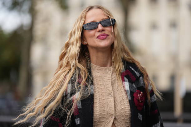 Guest wears sunglasses, a long beige wool cardigan, a gray black and red long jacket, outside Chanel, during the Womenswear Spring/Summer 2024 as...