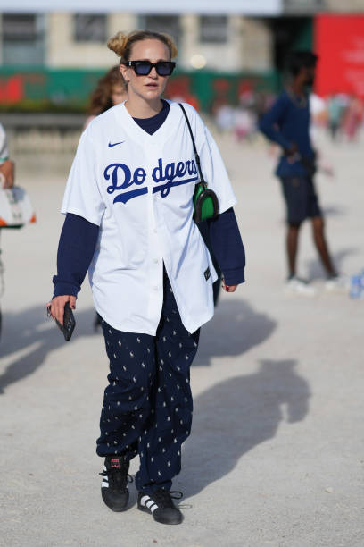 Guest wears sunglasses, a Nike baseball Dodgers shirt, a blue pulllover, navy blue flowing pants with printed details, sneakers, outside Casablanca,...