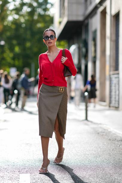 Guest wears sunglasses, a red cardigan , a Gucci detail, a short on-knee slit brown skirt, white kitten heels shoes, outside Bally, during the Milan...