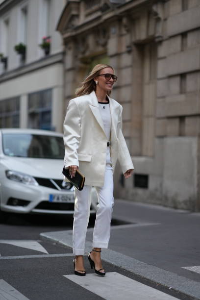 Guest wears sunglasses,, a white lustrous silk oversized blazer jacket, a white top from Courreges, white pants, pointed shoes, outside Alessandra...