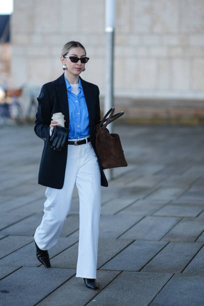 Guest wears sunglasses, earrings, a blue shirt, a white top, a black oversized blazer jacket , a belt, white pants , pointed black leather shoes, a...