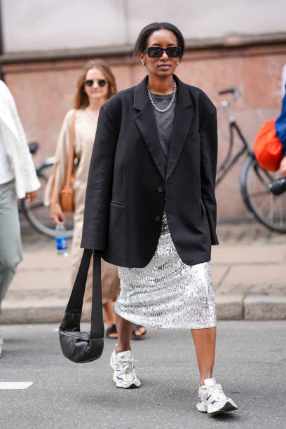 Guest wears sunglasses, earrings, a necklace, a gray t-shirt, a black oversized blazer jacket, a silver shiny sequined midi skirt, New Balance...