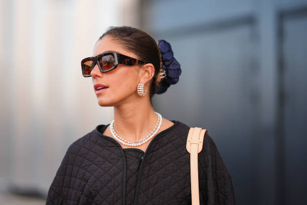 Guest wears sunglasses, golden earrings, a necklace , a scrunchie, a blue monogram logo printed Vuitton bag, a black oversized padded jacket ,...