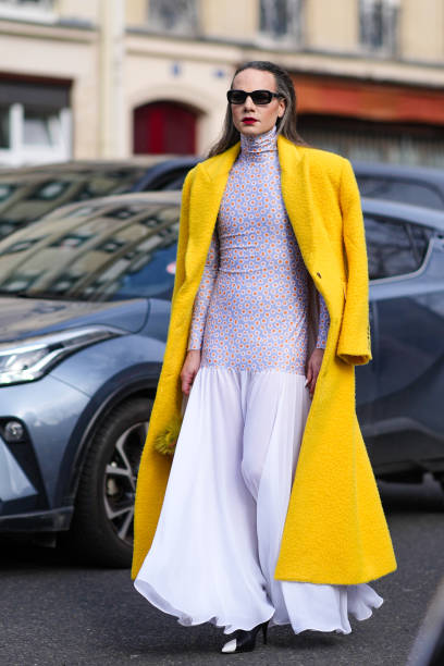 Guest wears sunglasses, red lipstick, a yellow fluffy long wool coat , a floral print turtleneck top / long dress with gathered bottom part, outside...