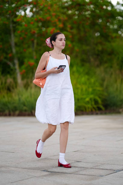 Guest wears white red scrunchie, bright pastel orange bag, white midi dress,white socks, dark red heeled ballerina leather shoes, outside Marimekko,...