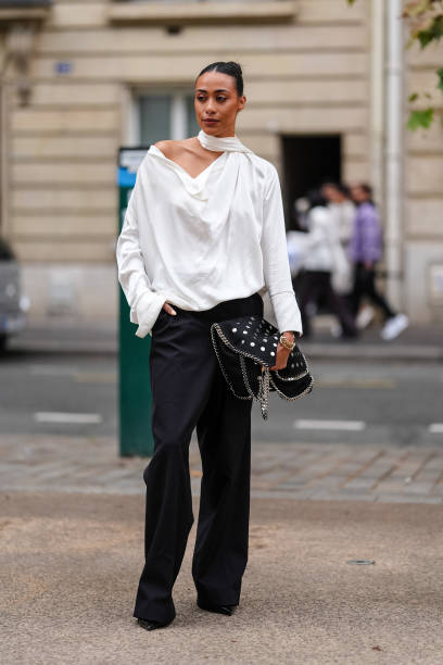 Guest wears white satin long sleeve half shoulder shirt, black loose pants, black Stella McCartney leather bag with silver detail, outside Stella...