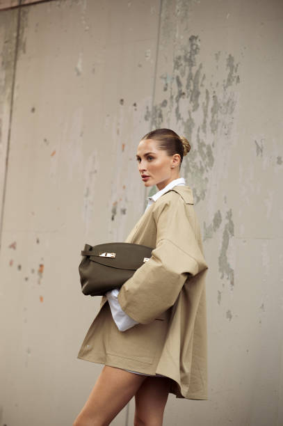 Guest wears white shirt, white skirt, beige coat and olive green bag outside Ferragamo show during the Milan Fashion Week Spring/Summer 2025 on...