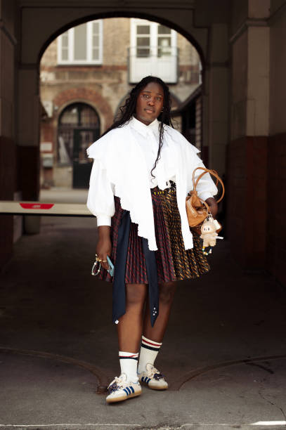 Guest wears white shirt, white socks, sneakers, pleated colourful skirt and brown bag outside Stem presentation during the Copenhagen Fashion Week...