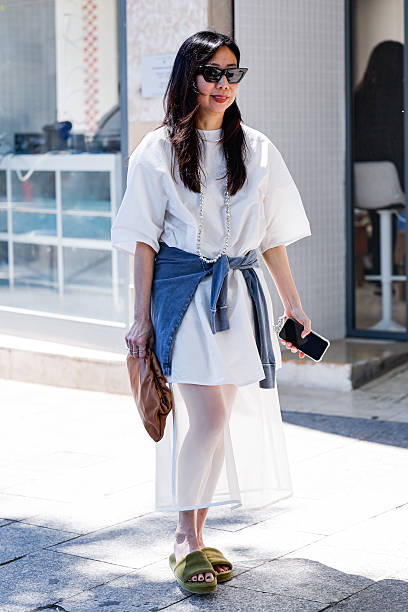 Guest wears white t-shirt, white sheer midi skirt, denim shirt on the waist, green sandals, brown pouch bag, outside Kartik Research, during the...