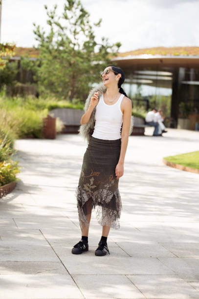 Guest wears white tank top, black skirt, black socks, black sneakers, green bag with fur and sunglasses outside the Marimekko show during day four of...
