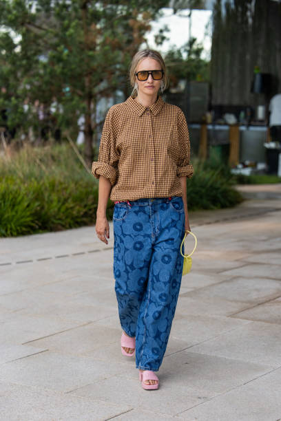 Guest wears yellow houndstooth button shirt, denim jeans with print, yellow bag outside Marimekko during day four of the Copenhagen Fashion Week SS25...