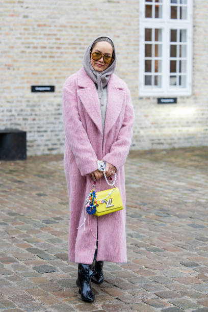 Guest wears yellow Louis Vuitton bag, pink coat, grey hoody outside Munthe during the Copenhagen Fashion Week Autumn/Winter 2025 on January 30, 2025...