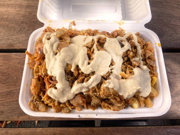 halal chicken and potato chips snack pack with tahini sauce in a cardboard takeout container on a wooden outdoor table - junk food stock pictures, royalty-free photos & images