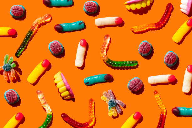 halloween jelly beans, finger-shaped, brains, worm and vampire teeth on orange background - junk food stock pictures, royalty-free photos & images