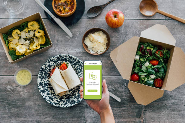 hand holding smartphone, vegetarian takeaway food on dining table - junk food stock pictures, royalty-free photos & images