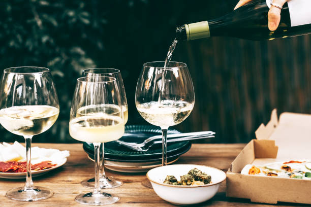 hand pouring white wine into elegant glasses set on a wooden table with appetizers, perfect for a social gathering or celebration. - garden decoration stock pictures, royalty-free photos & images