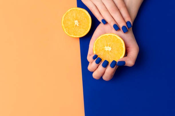 hand with artificial manicured nails colored with blue and orange nail polish on textile background - nails art stock pictures, royalty-free photos & images