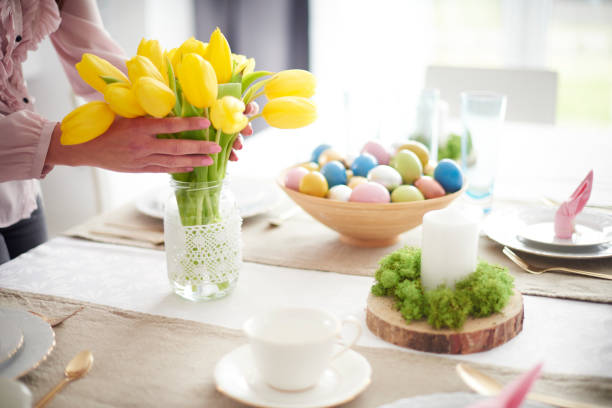 hands of woman arranging yellow tulips at easter dining table - home decoration stockfoto's en -beelden