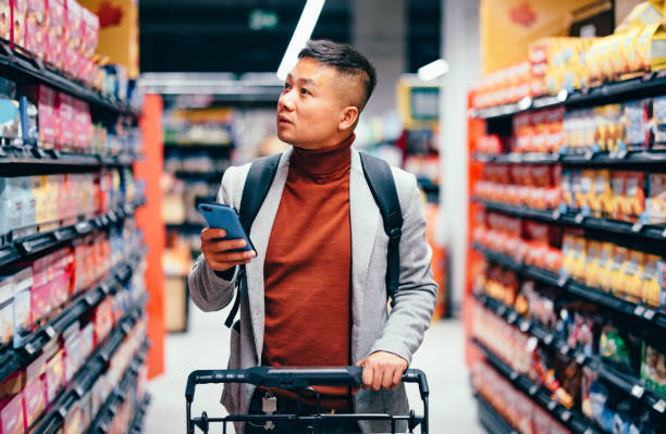 handsome asian male searching for groceries from the list on his mobile phone - food stock pictures, royalty-free photos & images