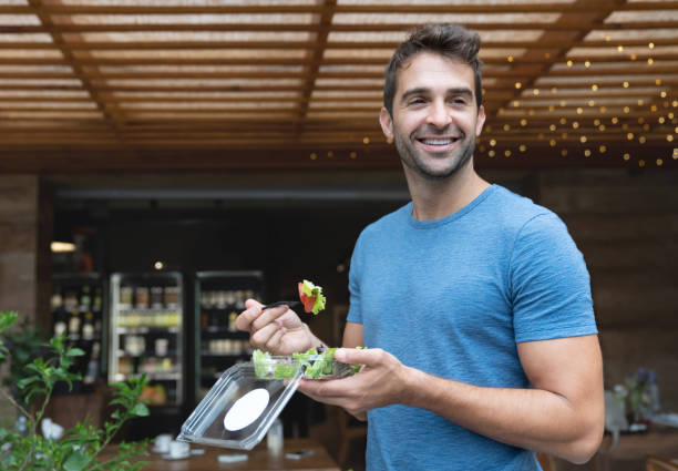 handsome man eating a salad on the go - junk food stock pictures, royalty-free photos & images