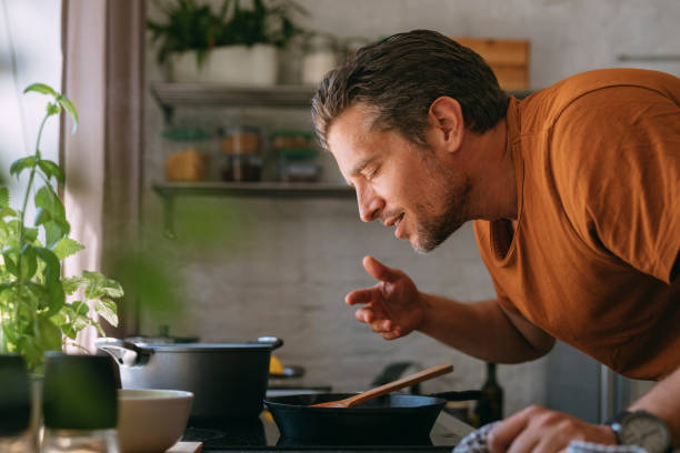 handsome young man enjoying the aroma of a meal in a kitchen - food stock pictures, royalty-free photos & images