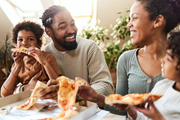 happy african american family communicating while having pizza for lunch at home. - junk food stock pictures, royalty-free photos & images